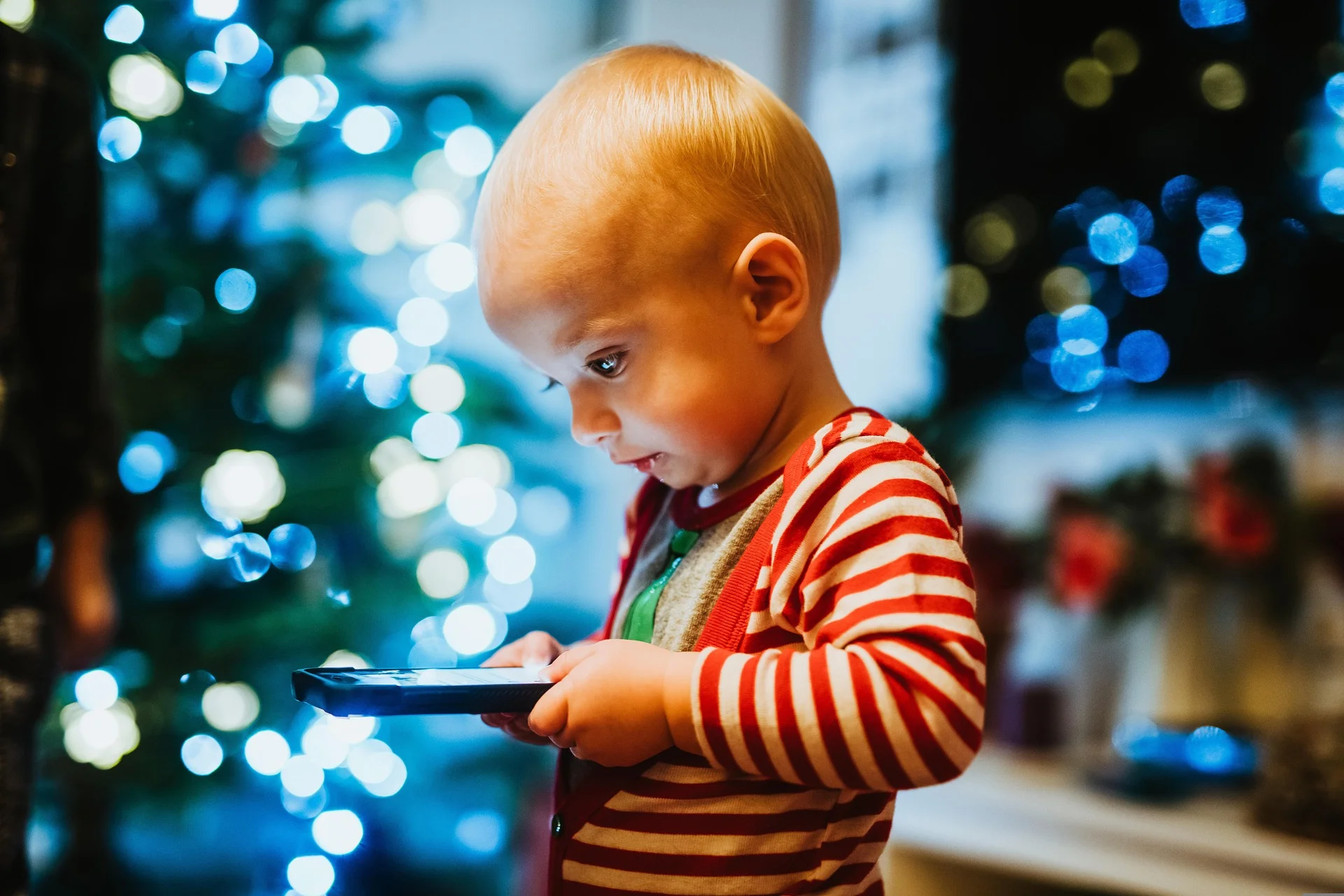 Dziecko trzyma telefon przy uchu, siedząc przy oknie